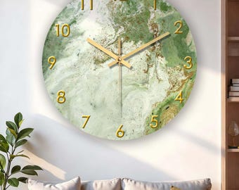 May include: Round wall clock with a green and white marbled design. The clock face features gold-colored numerals and hands. The clock is hanging on a white wall above a sofa with pillows.