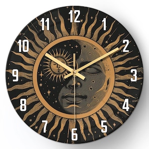 May include: Round wall clock with a black face featuring a gold sun and moon design. The clock has gold hands and white numerals. The sun and moon are in the center, surrounded by a gold border and a black background.