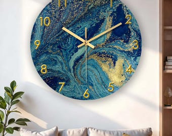 Puede incluir: Un reloj de pared redondo con un diseño de mármol azul y dorado. La esfera del reloj tiene números y manecillas doradas. El reloj está colgado en una pared blanca sobre un sofá con cojines neutros.