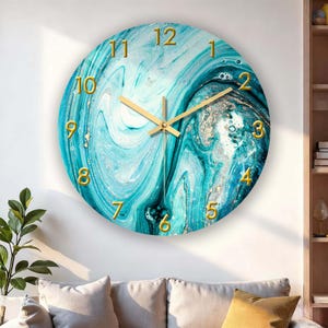 May include: Round wall clock with a turquoise and white marble design. The clock face features gold-colored numerals and hands. The clock is mounted on a white wall, with a sofa and plant visible in the foreground.