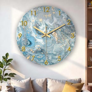 May include: Round wall clock with a blue and gold marble design. The clock face features gold numerals and hands, with a marbled blue and gold background. The clock is mounted on a white wall.