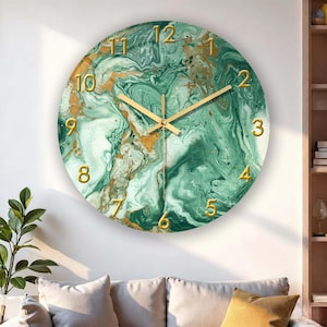 May include: Circular wall clock with a green and gold marble effect. The clock face has gold numerals and hands. It's mounted on a white wall above a sofa with neutral cushions. A decorative item for the home.