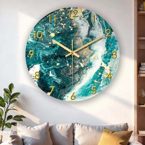 May include: Round wall clock with a teal, white, and gold marbled design. The clock face features gold numerals and hands. The clock is mounted on a white wall, with a glimpse of a sofa and plant in the foreground.