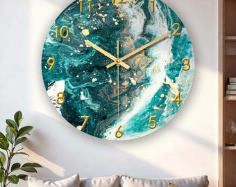 Puede incluir: Reloj de pared redondo con un diseño veteado en tonos turquesa, blanco y dorado. La esfera del reloj presenta números y manecillas doradas. El reloj está montado en una pared blanca, con un sofá y una planta en primer plano.