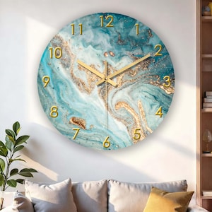 Puede incluir: Reloj de pared redondo con diseño de mármol azul y dorado. La esfera del reloj tiene números y manecillas doradas. El reloj está montado en una pared blanca sobre un sofá con cojines beige.