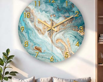 Puede incluir: Reloj de pared redondo con diseño de mármol azul y dorado. La esfera del reloj tiene números y manecillas doradas. El reloj está montado en una pared blanca sobre un sofá con cojines beige.