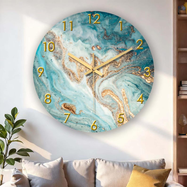 May include: Round wall clock with a blue and gold marble design. The clock face features gold numerals and hands. The clock is mounted on a white wall above a sofa with beige cushions.