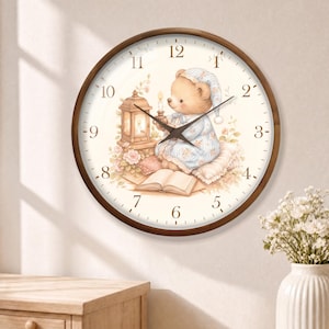 May include: A round wall clock with a dark brown wooden frame and a cream-colored face. The clock features black hands and brown numerals. The center illustration depicts a teddy bear in blue pajamas holding a candle near a lantern and book.