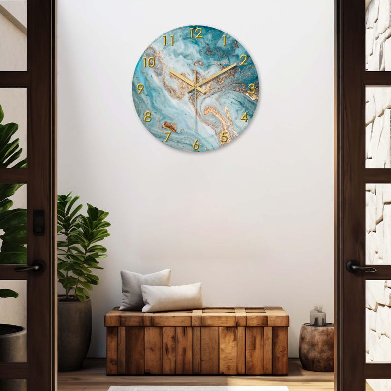 May include: A round wall clock with a blue and gold marble design. The clock has gold-colored numerals and hands. The clock is hanging on a white wall above a wooden bench.