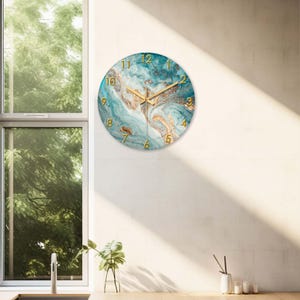 May include: A round wall clock with a teal and gold marble design. The clock face features gold numerals and hands. The clock is mounted on a white wall, with natural light from a nearby window.