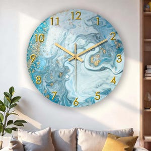 Könnte beinhalten: Runde Wanduhr mit blau-weißem Marmormuster. Das Zifferblatt hat goldfarbene Ziffern und Zeiger. Goldene Flecken sind über das Zifferblatt verstreut. Die Uhr hängt an einer weißen Wand.
