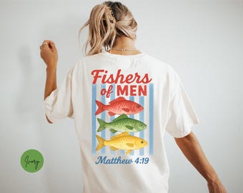 May include: Cream-coloured t-shirt with the text "Fishers of Men" in red and blue. The shirt features three colourful fish: red, green, and yellow. The text "Matthew 4:19" is below the fish.