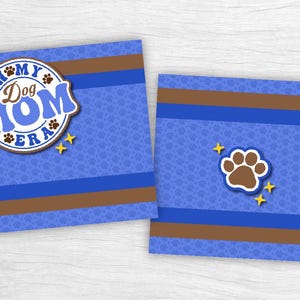 May include: Two blue square cards with a dog theme. One card features the text "In My Dog Mom Era" in a circular design with paw prints and stars. The other card has a paw print and stars.