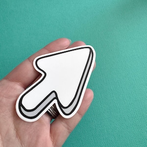 May include: A white arrow sticker with a black outline and a grey shadow effect. The arrow is held in a hand against a teal background. The arrow points up and to the right.