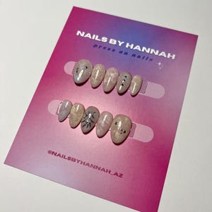 Puede incluir: Conjunto de diez uñas postizas con un diseño de mármol rosa y blanco. Algunas uñas tienen purpurina plateada y detalles negros. Las uñas se muestran en una tarjeta rosa y morada con el texto "NAILS BY HANNAH press on nails" y "@NAILSBYHANNAH_AZ".