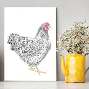 May include: A watercolor print of a chicken with gray and white speckled feathers, a red comb, and yellow feet. The artwork is displayed on a white canvas. A yellow teapot vase holds white flowers, adding a touch of color to the scene.