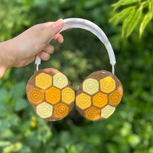 Puede incluir: Auriculares con cubiertas de oreja de ganchillo marr&oacute;n y amarillo con un patr&oacute;n de panal. Los auriculares tienen una diadema y auriculares blancos. Las cubiertas de las orejas est&aacute;n hechas de varios tonos de hilo amarillo y marr&oacute;n.