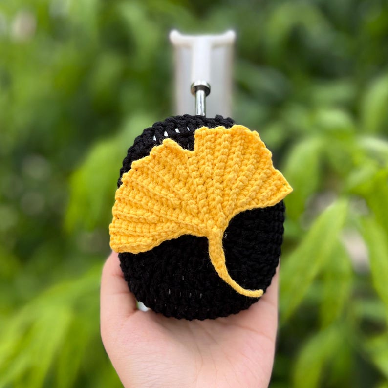 Pu&ograve; includere: Un design a forma di foglia di ginkgo all'uncinetto nero e giallo. La foglia &egrave; di colore giallo brillante ed &egrave; attaccata a un cerchio all'uncinetto nero. Il design &egrave; attaccato a un gancio di metallo argentato.