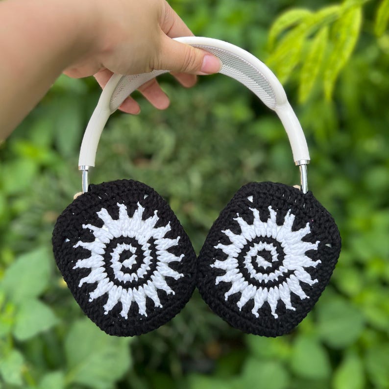 May include: White and silver headphones with black and white crochet ear covers. The ear covers feature a spiral sunburst design. The headband is white and the ear cups are black with a white sunburst pattern.