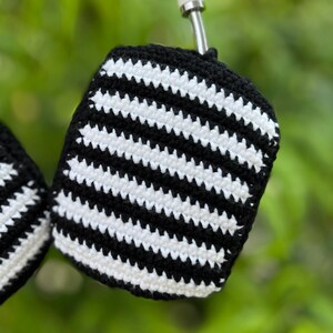 May include: Close-up of a black and white striped crochet item. The item is a small, rounded shape with a black border and a silver metal attachment. The crochet pattern features alternating black and white horizontal stripes.
