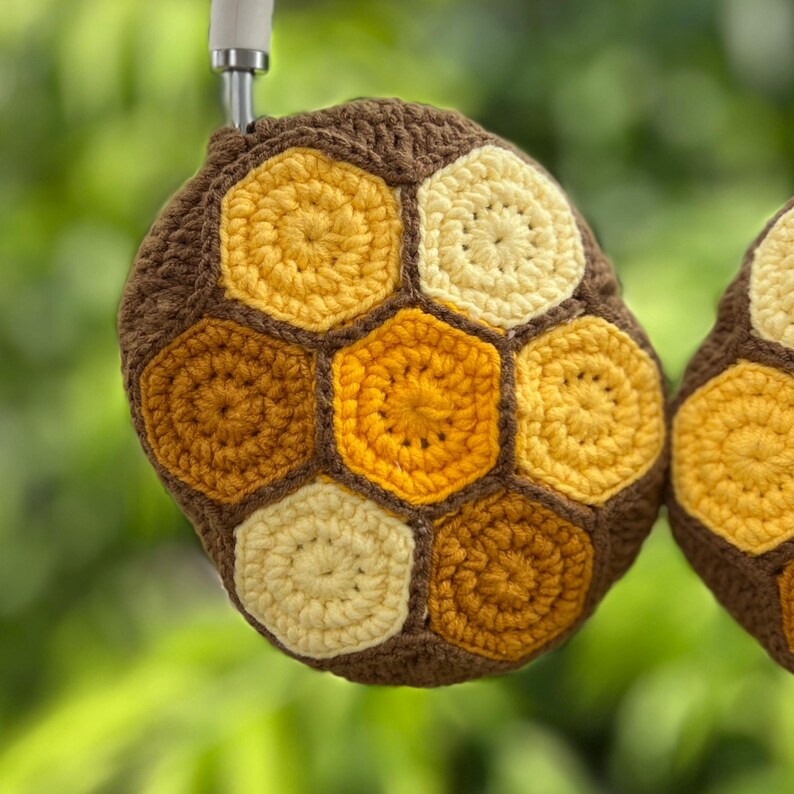 Puede incluir: Fundas de auriculares de ganchillo con un dise&ntilde;o de panal. Las fundas presentan un borde marr&oacute;n y formas hexagonales amarillas, doradas y crema. El dise&ntilde;o recuerda a una colmena de abejas, ofreciendo un accesorio &uacute;nico y hecho a mano.