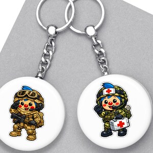 May include: Two white round keyrings with cartoon soldier designs. One shows a soldier with a rifle, the other a medic with a first aid kit. Both have silver chains and key rings.
