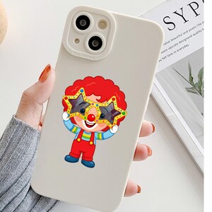 K&ouml;nnte beinhalten: Eine matte, cremewei&szlig;e Smartphone-H&uuml;lle mit einer Cartoon-Clown-Illustration. Der Clown hat leuchtend rotes Haar, eine rote Nase und tr&auml;gt eine gro&szlig;e, gelbe, sternf&ouml;rmige Brille. Er ist mit einem gestreiften Oberteil, einer roten Latzhose und blauen Schuhen bekleidet.