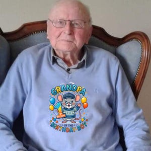 May include: A light blue sweatshirt with a graphic of a cartoon mouse wearing a hat and holding balloons. The text on the shirt reads "Grandpa of the Birthday Boy" with the number "1" on a balloon.