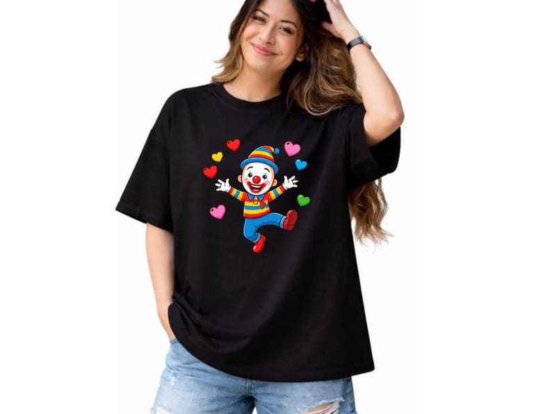 K&ouml;nnte beinhalten: Ein schwarzes T-Shirt mit kurzen &Auml;rmeln und einem Grafikdruck eines l&auml;chelnden Clowns, der einen gestreiften Hut und bunte Kleidung tr&auml;gt, umgeben von mehreren kleinen, mehrfarbigen Herzen in den Farben Rot, Gelb, Blau, Pink und Gr&uuml;n.