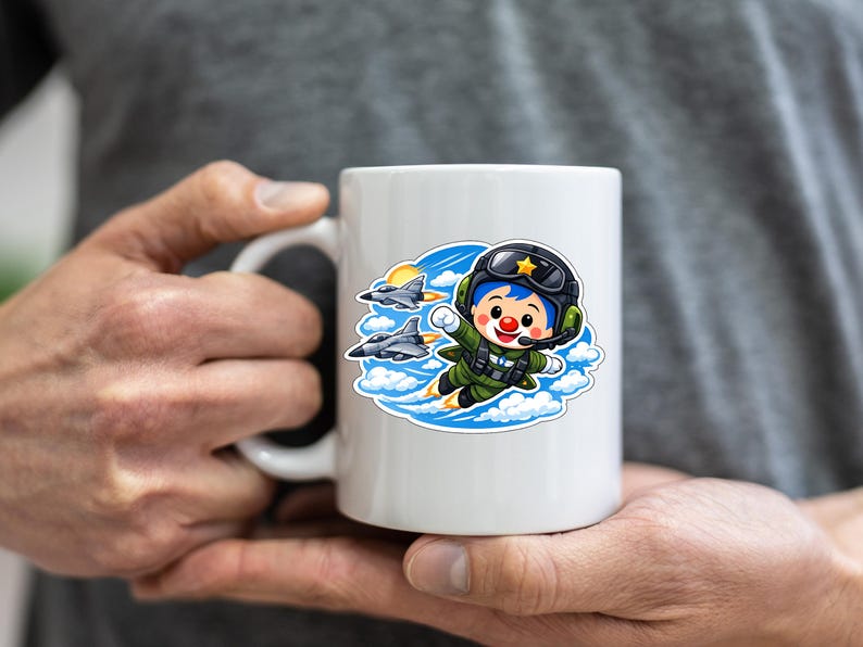 May include: White ceramic mug with a cartoon pilot illustration in a green flight suit, black helmet, and red clown nose. The design includes two fighter jets, clouds, and a sun. The mug is held by a person.