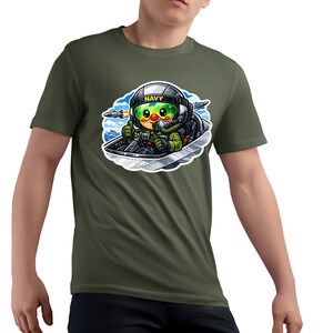 May include: Olive green t-shirt with a cartoon pilot in a fighter jet. The pilot wears a helmet with "NAVY" and a green visor. The graphic is detailed with blue, green, yellow, and black colours.