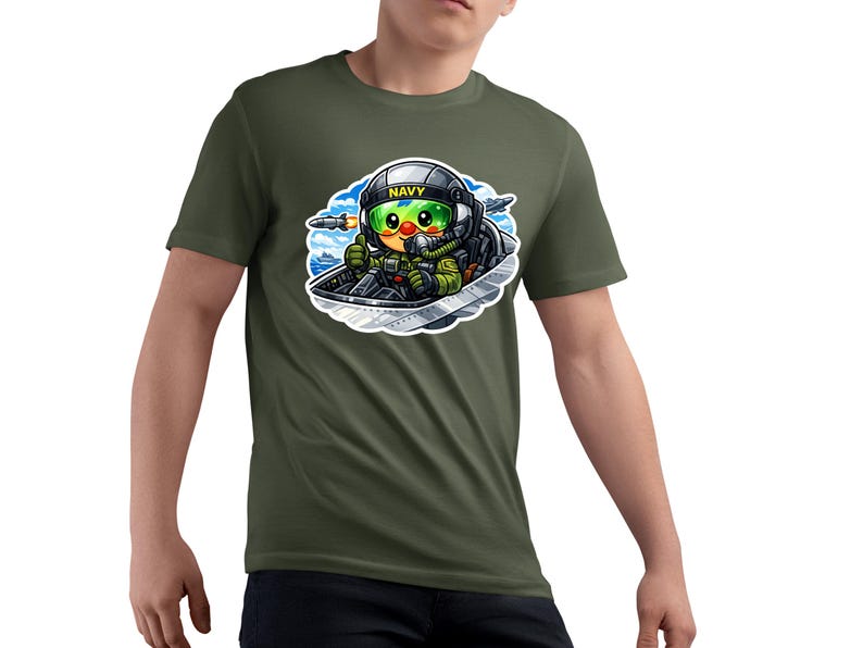 May include: Olive green t-shirt with a cartoon pilot in a fighter jet. The pilot wears a helmet with "NAVY" and a green visor. The graphic is detailed with blue, green, yellow, and black colours.