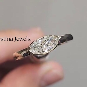 May include: A silver ring with a marquise-shaped diamond set in a simple band. The ring is held by a hand.