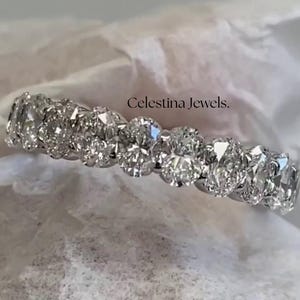 May include: A silver band with a row of round, clear diamonds set in a pave setting. The band is on a white surface. Celestina Jewels.