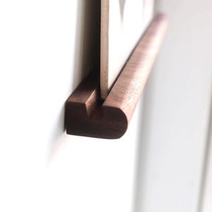 May include: A dark brown wooden display ledge with a horizontal groove running along the top surface. A thin, flat, light-colored rectangular board is inserted vertically into the groove, held securely in place by the wooden structure.