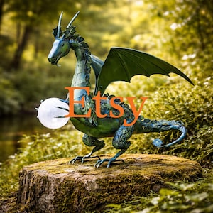 May include: A detailed, green and blue dragon sculpture holding a glowing orb. The dragon has large wings and is perched on a moss-covered tree stump. The word "Etsy" is displayed in orange across the image.