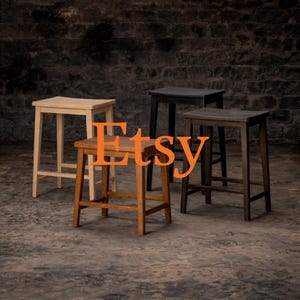 May include: Four wooden bar stools in varying shades of brown and black are arranged in front of a dark brick wall. The word "Etsy" is superimposed in orange over the stools. The stools have square seats and four legs.