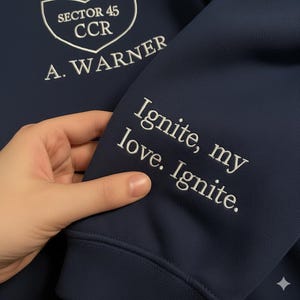 May include: Dark blue sweatshirt with white embroidered lettering. The upper left chest has a crest with "SECTOR 45 CCR" and "A. WARNER". The right sleeve reads "Ignite, my love. Ignite."