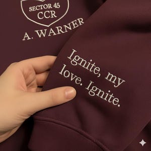 May include: A maroon sweatshirt with white embroidered text and a shield logo. The sleeve features the text "Ignite, my love. Ignite." The chest displays "Sector 45 CCR" and "A. Warner" in white.