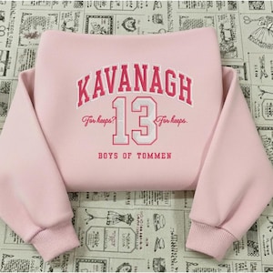 Puede incluir: Una sudadera rosa claro con el nombre "KAVANAGH" arqueado en rojo y blanco, con el número "13" debajo. El texto "For keeps?" y "For keeps." flanquean el número. Las palabras "BOYS OF TOMMEN" están debajo.
