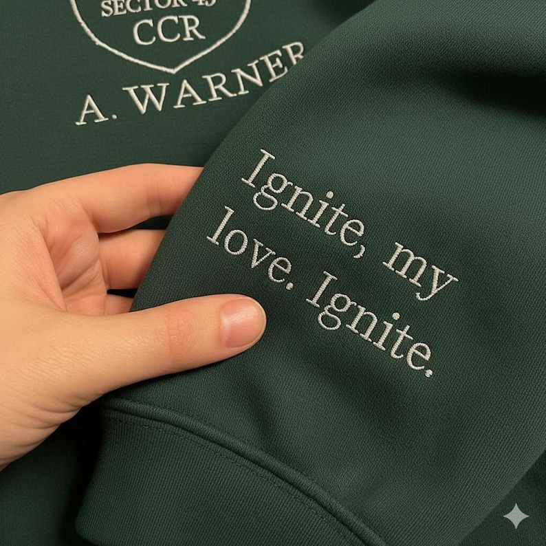 May include: Dark green hoodie with white embroidered text on the sleeve that reads "Ignite, my love. Ignite." The upper left has white embroidered text that reads "Sector 45 CCR" and "A. Warner".