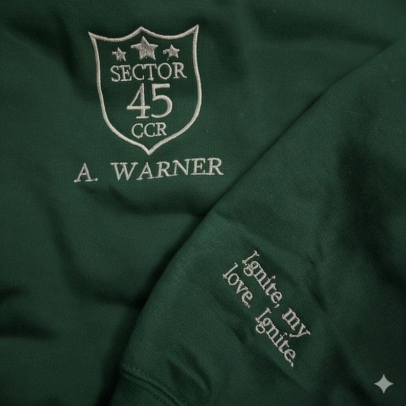 May include: Dark green sweatshirt with white embroidered text and design. The design includes a shield with "SECTOR 45 CCR" and "A. WARNER". The sleeve features the text "Ignite, my love. Ignite."