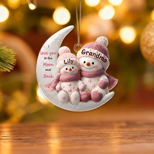 Może przedstawiać: Ozdoba dekoracyjna z dwoma bałwanami na księżycu. Bałwany mają na sobie różowe czapki i szaliki, z napisami "Grandma" i "Lily". Księżyc ma napis "Love you to the Moon and Back".