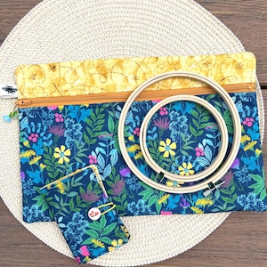 May include: A navy blue floral print craft organiser set with a matching small wallet and two wooden embroidery hoops. The organiser has a yellow top with a zip and a bee-themed design. The wallet has a button closure.