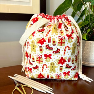 May include: A white drawstring bag with a red and gold Christmas pattern. The bag features gingerbread men, candy canes, presents, and poinsettias. The bag is made of fabric and has a white cotton drawstring.
