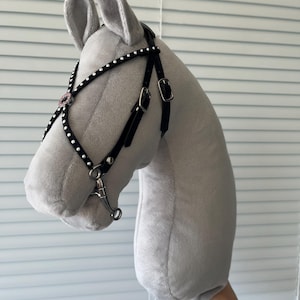 May include: A plush grey horse head toy featuring a black bridle with white stud accents, silver-toned metal buckles, and a silver-toned metal bit. The horse head is crafted from a soft, smooth fabric and is designed for play or display purposes.