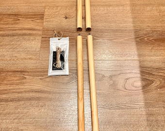 May include: Four light-colored wooden dowels with smooth cylindrical surfaces, arranged in two pairs. Two dowels feature threaded metal ends for assembly. A small, clear plastic bag contains a length of brown twine for hanging purposes.