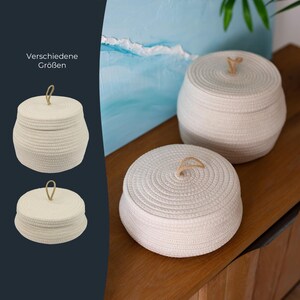 May include: Two round, off-white woven rope storage baskets with matching lids, each featuring a small tan rope loop handle on top. The image includes a dark sidebar with the text "Verschiedene Größen" and two smaller basket icons.