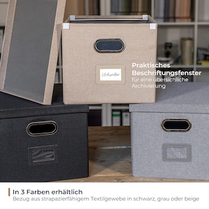 Könnte beinhalten: Eine Auswahl an Stoff-Aufbewahrungsboxen in Schwarz, Grau und Beige. Jede Box hat ein Etikettenfenster und einen Metallgriff. Der Text auf den Boxen lautet "Urkunden" und "Praktisches Beschriftungsfenster für eine übersichliche Archivierung."