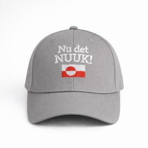 Puede incluir: Gorra de b&eacute;isbol gris con el texto "Nu det NUUK!" bordado en blanco sobre un peque&ntilde;o dise&ntilde;o de bandera. La bandera presenta un rect&aacute;ngulo rojo con un c&iacute;rculo blanco y un punto rojo.